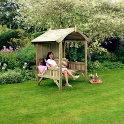 Deluxe wooden garden gazebo with a sitting bench, surrounded by lush greenery and colorful flowers, ideal for relaxing outdoor leisure and garden parties.