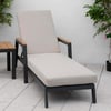 Modern outdoor lounge chair with beige cushion, wooden armrests, and black metal frame, set on a patio with pink flowering plants for stylish garden relaxation.