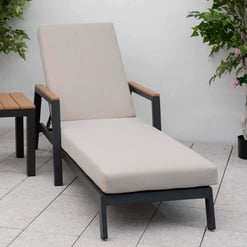 Modern outdoor lounge chair with beige cushion, wooden armrests, and black metal frame, set on a patio with pink flowering plants for stylish garden relaxation.
