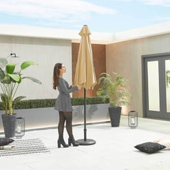 Modern outdoor patio with beige umbrella, lush potted plants, and stylish decor, perfect for relaxing and entertaining in backyard or garden space.