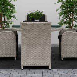 Elegant outdoor patio table and wicker chairs with black cushions, surrounded by lush green plants, perfect for home garden decor and outdoor dining setups.