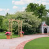 Beautiful landscaped backyard with garden gazebo, wooden archway, blooming flowers, and lush green trees, perfect for outdoor relaxation and entertaining.