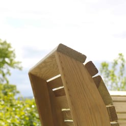 Natural wood outdoor furniture, including a wooden chair with slatted design, set against a lush green background and a partly cloudy sky. Perfect for garden or patio relaxation.