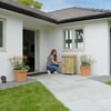 Plant care and gardening at a modern white house patio, featuring potted flowers and a woman tending to her garden, emphasizing home gardening and outdoor landscaping.