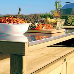 Fresh outdoor catering station with a bowl of pasta, colorful skewers, and a chafing dish set against a scenic vineyard backdrop for garden entertaining.