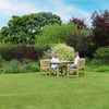 Bright outdoor garden scene with two women enjoying a sunny day at a wooden table surrounded by lush trees and colorful flowering plants, perfect for outdoor living and garden furniture.