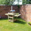 Outdoor barbecue station with brick wall backdrop and lush green grass, perfect for backyard entertaining and garden events.