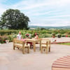 Bright outdoor patio with wooden dining furniture, lush garden backdrop, scenic countryside views, and decorative potted plants for garden enhancement.