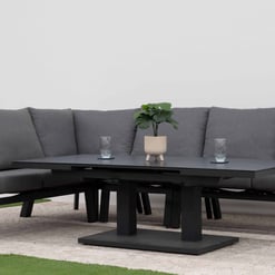 Modern outdoor sectional sofa set with dark gray cushions and black metal frame, perfect for garden or patio entertaining, featuring a sleek coffee table with decorative plants and glasses.
