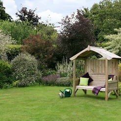 Garden with a wooden garden bench with canopy and colorful cushions, surrounded by lush flowering plants and trees, ideal for outdoor relaxation and garden décor.
