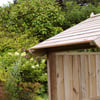 Nature-inspired wooden garden shed with a sloped roof, surrounded by lush greenery and flowering plants, perfect for outdoor storage and enhancing your garden's aesthetic.