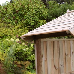 Nature-inspired wooden garden shed with a sloped roof, surrounded by lush greenery and flowering plants, perfect for outdoor storage and enhancing your garden's aesthetic.