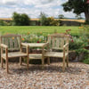 Natural wooden garden chairs on a gravel surface with colorful flower beds and lush green lawn, ideal for outdoor relaxation and garden decor.