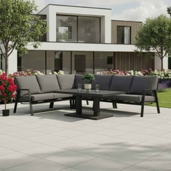 Modern outdoor patio furniture set with a black metal sectional sofa and coffee table, surrounded by landscaped garden with vibrant flowers and trees, ideal for outdoor living and garden design.
