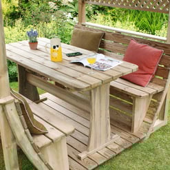 Rustic wooden outdoor dining set with benches under a garden gazebo, surrounded by lush greenery and blooming flowers. Perfect for garden gatherings and outdoor entertaining.