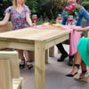 Natural wooden outdoor dining table with women enjoying a garden gathering, featuring wine glasses and a cheese platter, perfect for garden furniture and outdoor entertaining.