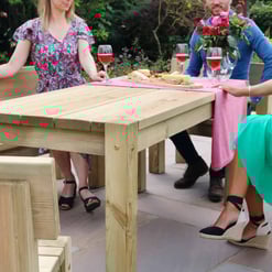 Natural wooden outdoor dining table with women enjoying a garden gathering, featuring wine glasses and a cheese platter, perfect for garden furniture and outdoor entertaining.