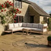 Elegant outdoor patio seating with comfortable cream cushions and light wooden furniture set against a rustic stone house and lush garden setting.