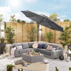 Modern outdoor patio with cushioned sectional sofa, stylish throw pillows, and a large patio umbrella, surrounded by lush plants and garden decor for an inviting backyard living space.
