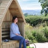 Wooden garden house with a woman sitting, eco-friendly outdoor garden decor, perfect for outdoor relaxation, gardening, or backyard setup. Crafted from natural wood, ideal for enhancing garden aesthetics.