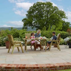 Warm wooden outdoor patio furniture set on a stone terrace, overlooking lush garden and scenic countryside, perfect for outdoor dining and family gatherings.