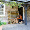 A woman stacking firewood under a covered stone porch of a rustic home with garden decor.