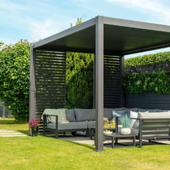 Stylish outdoor pergola with modern black slatted walls and comfortable gray sectional sofa, perfect for outdoor relaxation and garden entertaining at Empire Home and Garden.