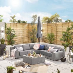 Stylish outdoor patio with cozy gray sectional sofa, decorative pillows, lush green plants, modern lanterns, and a privacy wooden fence, perfect for relaxing outdoor living.