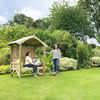 A peaceful garden scene with two women enjoying outdoor relaxation, surrounded by lush greenery, flowering plants, and a wooden garden bench under a small pergola. Ideal for outdoor living and garden decor.