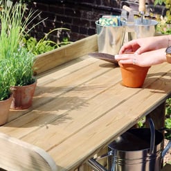 Bright outdoor gardening tools and plant pots on wooden garden work table, with gardening supplies and vibrant plants in the background.