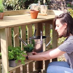 Potted herbs on a wooden garden cart in a lush outdoor garden scene, perfect for outdoor gardening and plant care enthusiasts.