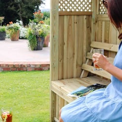 Cozy outdoor garden seating area with a woman relaxing, enjoying a glass of drink, surrounded by vibrant potted flowers and lush greenery, perfect for outdoor living and garden relaxation.
