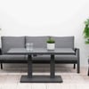 Lounge outdoor patio furniture set with grey cushioned chairs and sofa, surrounded by lush green plants and flowering shrubs for a stylish garden or backyard entertainment space.