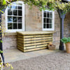 Stylish wooden outdoor storage box placed on a stone patio beside a rustic stone house with white-framed windows, surrounded by lush greenery and potted plants.