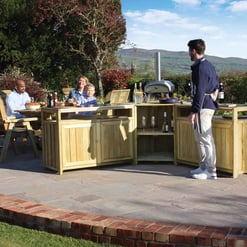 Garden outdoor kitchen and dining area with a wooden bar, barbecue grill, and happy family enjoying a meal in a scenic backyard setting.