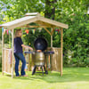 Dream backyard grill station with wooden shelter and festive bunting amidst lush greenery, perfect for outdoor cooking and gatherings.