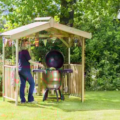 Dream backyard grill station with wooden shelter and festive bunting amidst lush greenery, perfect for outdoor cooking and gatherings.