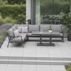 Modern outdoor patio furniture set with gray cushioned sectional and matching table, surrounded by lush greenery in a contemporary backyard setting.