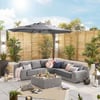 Modern outdoor patio with a large L-shaped grey sectional sofa, stylish throw pillows, a matching coffee table, lush potted plants, a black patio umbrella, and decorative lanterns in a private backyard setting.