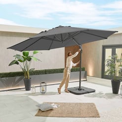 Stylish outdoor patio with a large gray patio umbrella, potted plants, lanterns, and a cozy rug, perfect for garden and outdoor living space enhancements.