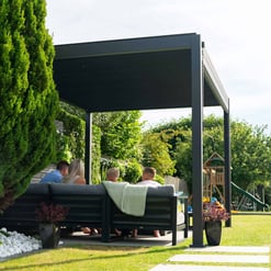 Modern outdoor patio with black pergola, comfortable seating, lush greenery, and backyard play area, ideal for relaxing and entertaining in your home and garden setting.
