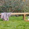 Relaxing outdoor garden bench with a cozy blanket, wine, and glasses on a wooden tray, surrounded by lush greenery, perfect for outdoor leisure and garden decor.