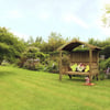 Elegant garden seating area with a wooden gazebo, lush greenery, and vibrant flowering plants, perfect for outdoor relaxation and enhancing garden aesthetics.