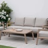 Stylish outdoor patio furniture set featuring a beige cushioned sofa and armchairs with wooden frames, surrounded by lush greenery and flowering plants for a serene garden retreat.