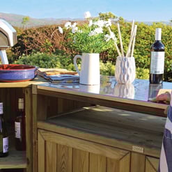 Bright outdoor gardening and entertaining space featuring a wooden bar with wine bottles, glasses, fresh flowers, and a grill, perfect for outdoor kitchen and garden design.