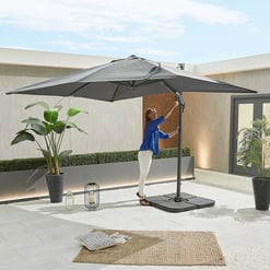 Outdoor patio with a large grey umbrella, potted plants, and cozy decor, perfect for backyard relaxation and entertaining with stylish garden furniture from Empire Home and Garden.