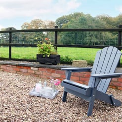 Cozy outdoor patio with Adirondack chair, flower tray, and lush green countryside view, perfect for relaxing and enjoying garden scenery or outdoor leisure at Empire Home and Garden.