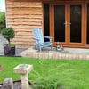 Rustic garden shed with wooden double doors, cozy outdoor seating with Adirondack chair, potted plants, and landscaped lawn. Perfect for garden storage and outdoor relaxation.