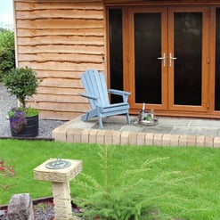 Rustic garden shed with wooden double doors, cozy outdoor seating with Adirondack chair, potted plants, and landscaped lawn. Perfect for garden storage and outdoor relaxation.
