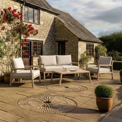 Elegant outdoor patio furniture set with cream cushioned seating next to a historic stone house, perfect for garden relaxation and summer gatherings.